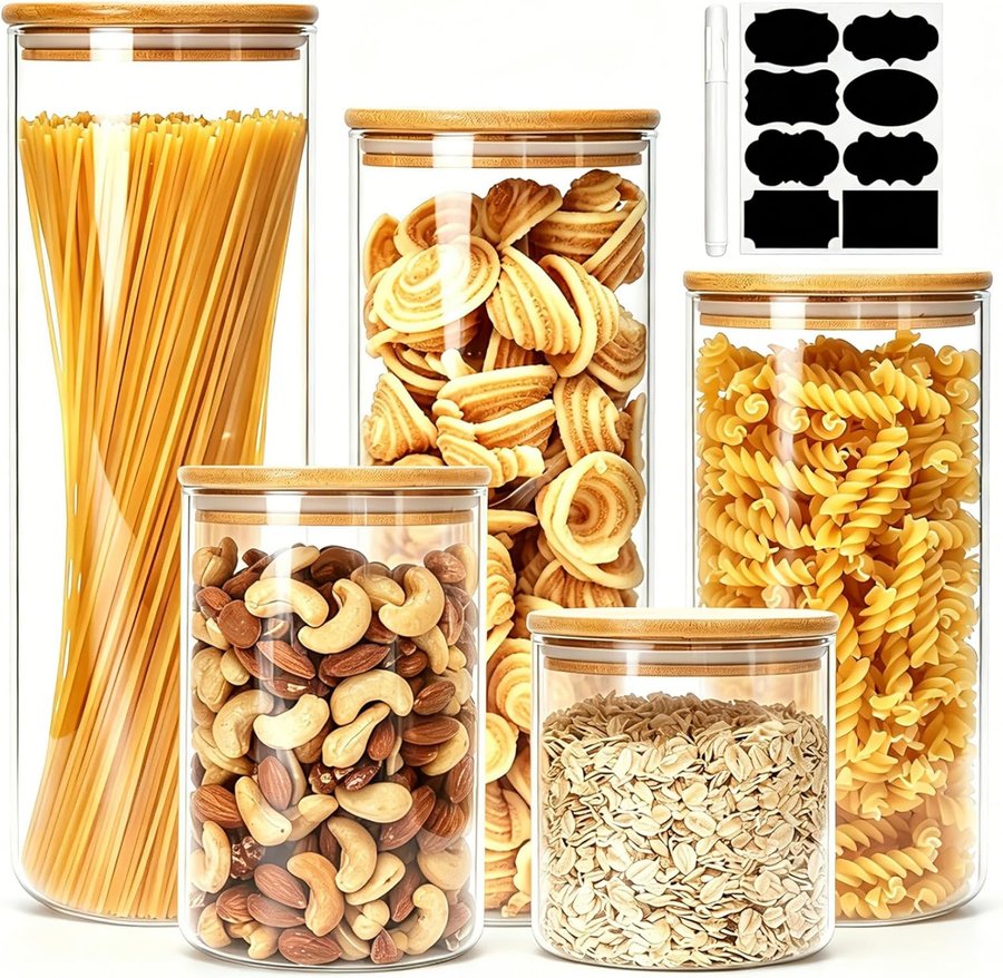 Five airtight glass jars with bamboo lids filled with pasta, nuts and oats